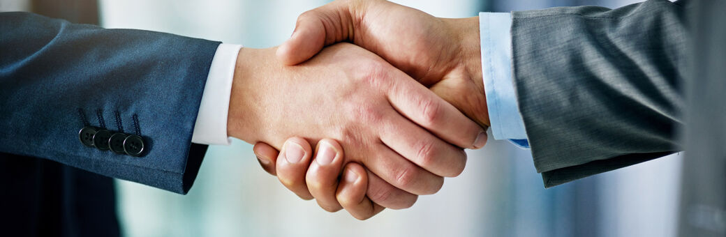 Two individuals wearing professional attire shaking hands. The image is a close-up on just the hands with a blurred background.