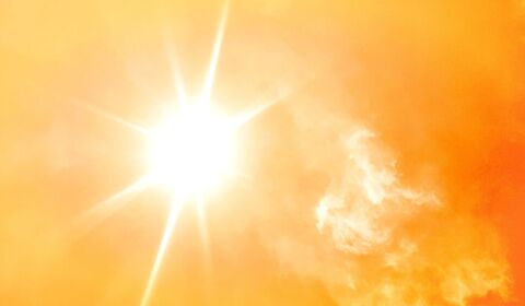 Bright sun emitting rays against a warm orange sky with soft, wispy clouds