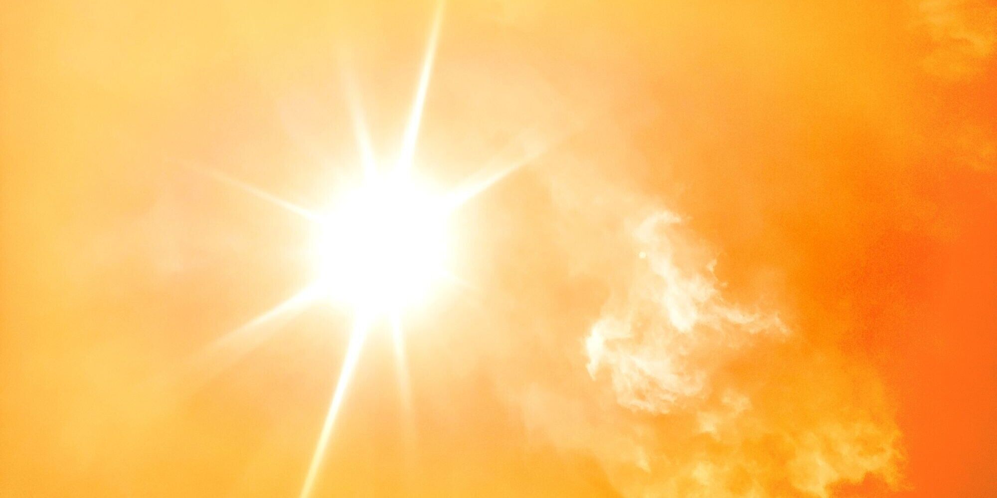Bright sun emitting rays against a warm orange sky with soft, wispy clouds