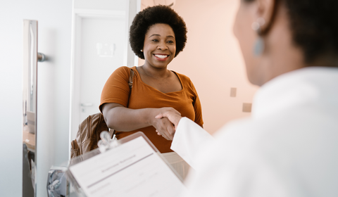 Smiling woman shaking hands with a healthcare professional at a clinic reception desk.