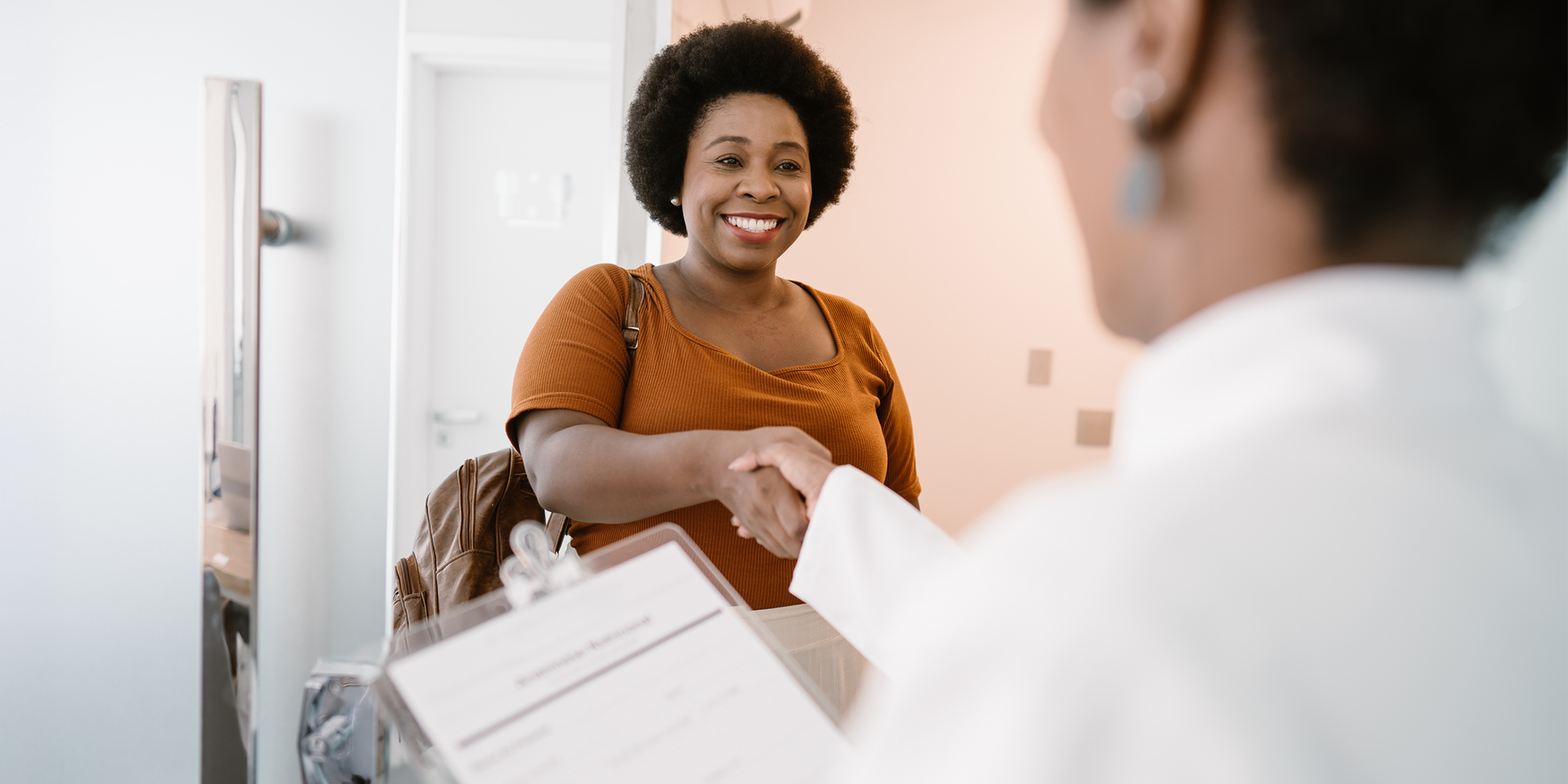 Smiling woman shaking hands with a healthcare professional at a clinic reception desk.