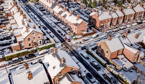 A snowy aerial view of a residential neighborhood with rows of brick houses and cars lining the streets.