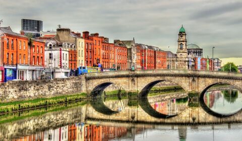 Stone bridge over river with colorful historic buildings and clock tower in the background.