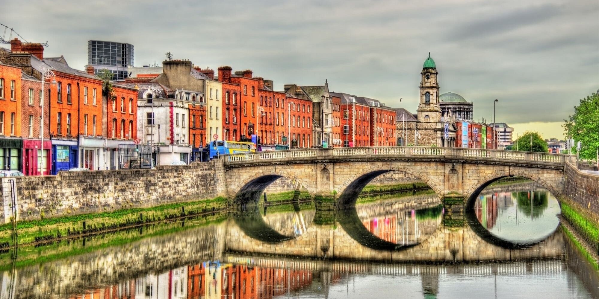 Stone bridge over river with colorful historic buildings and clock tower in the background.