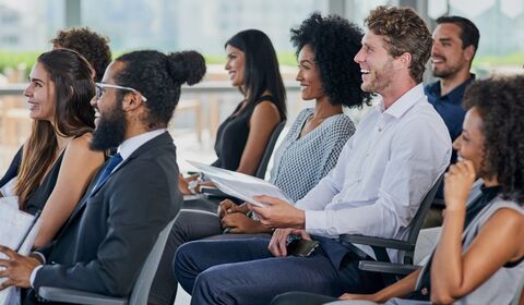 A group of people seated in a conference setting, attentively listening and taking notes during a presentation
