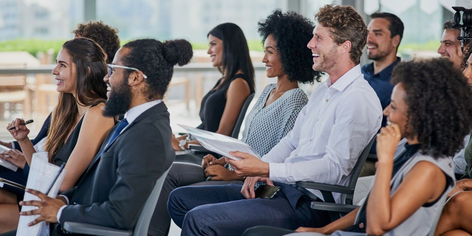 A group of people seated in a conference setting, attentively listening and taking notes during a presentation