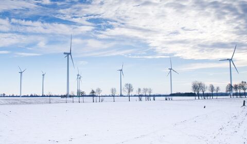 Wind turbines standing in a snowy field under a partly cloudy sky.