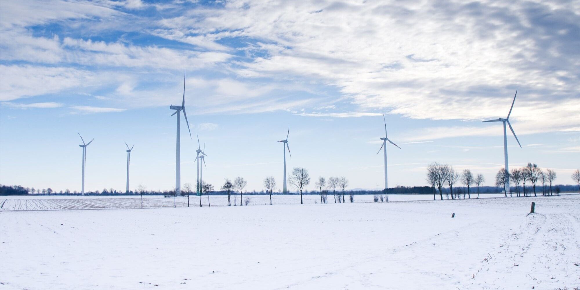 Wind turbines standing in a snowy field under a partly cloudy sky.