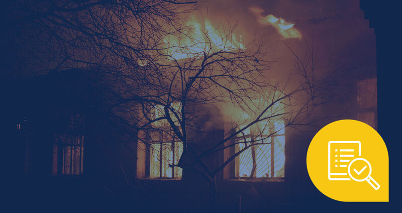 A building engulfed in flames at night, with bright orange fire contrasting against the dark silhouette of nearby trees
