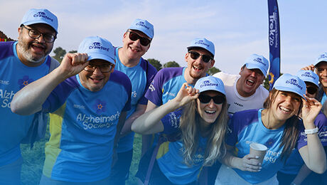 A group of people wearing matching blue shirts and caps, smiling and posing for the camera at an outdoor event