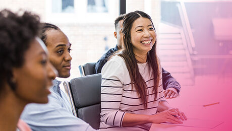 A diverse group of people seated at a conference table, engaging in a discussion, with one person smiling brightly