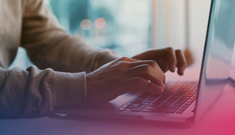 A person typing on a laptop with their hands in focus, soft lighting, and a blurred background