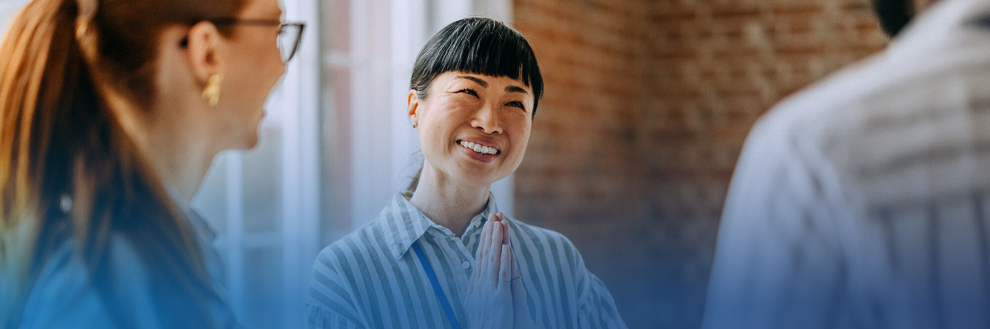 A person with a friendly smile and hands together in a welcoming gesture, engaged in conversation with two others
