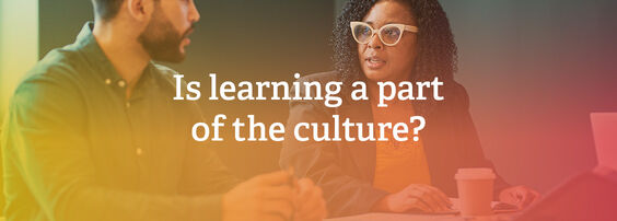 Two people engaged in a discussion at a table, with one asking, "Is learning a part of the culture?" A coffee cup is visible