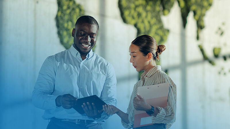 Two individuals discuss a digital tablet, with a world map in the background, conveying a collaborative work environment