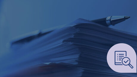 A stack of papers with a pen on top, accompanied by a magnifying glass icon on the bottom right