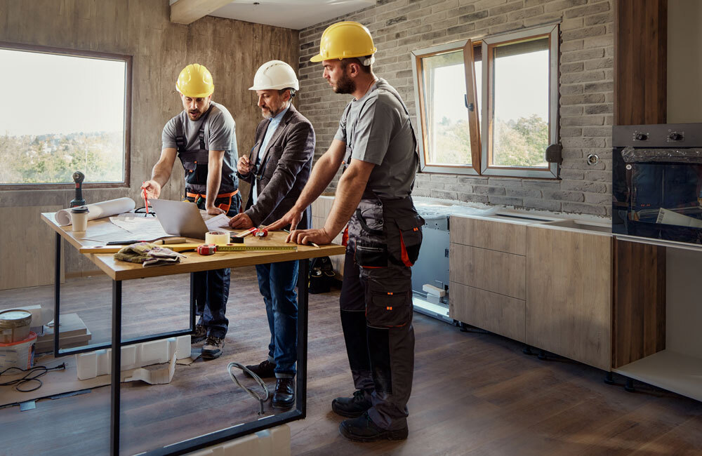 Construction team reviewing plans around a worktable inside a kitchen renovation site.